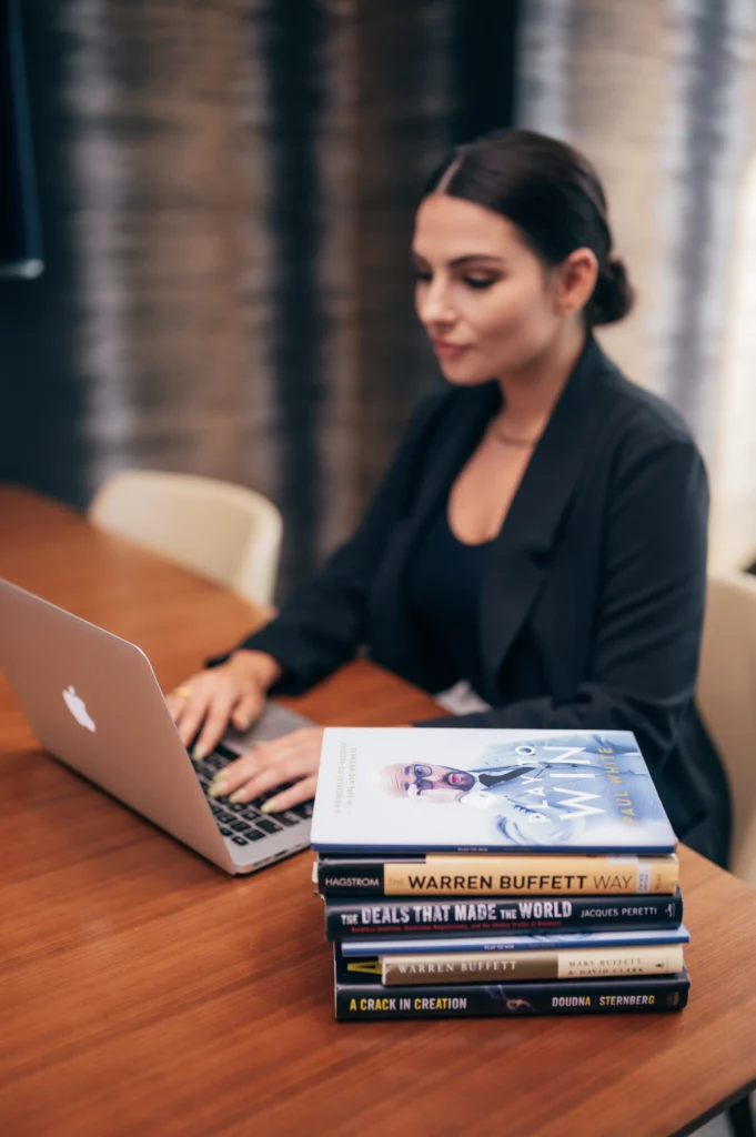Femme en costume noir travaillant sur un ordinateur. Livres présents sur le bureau avec comme sujet le Growth Hacking